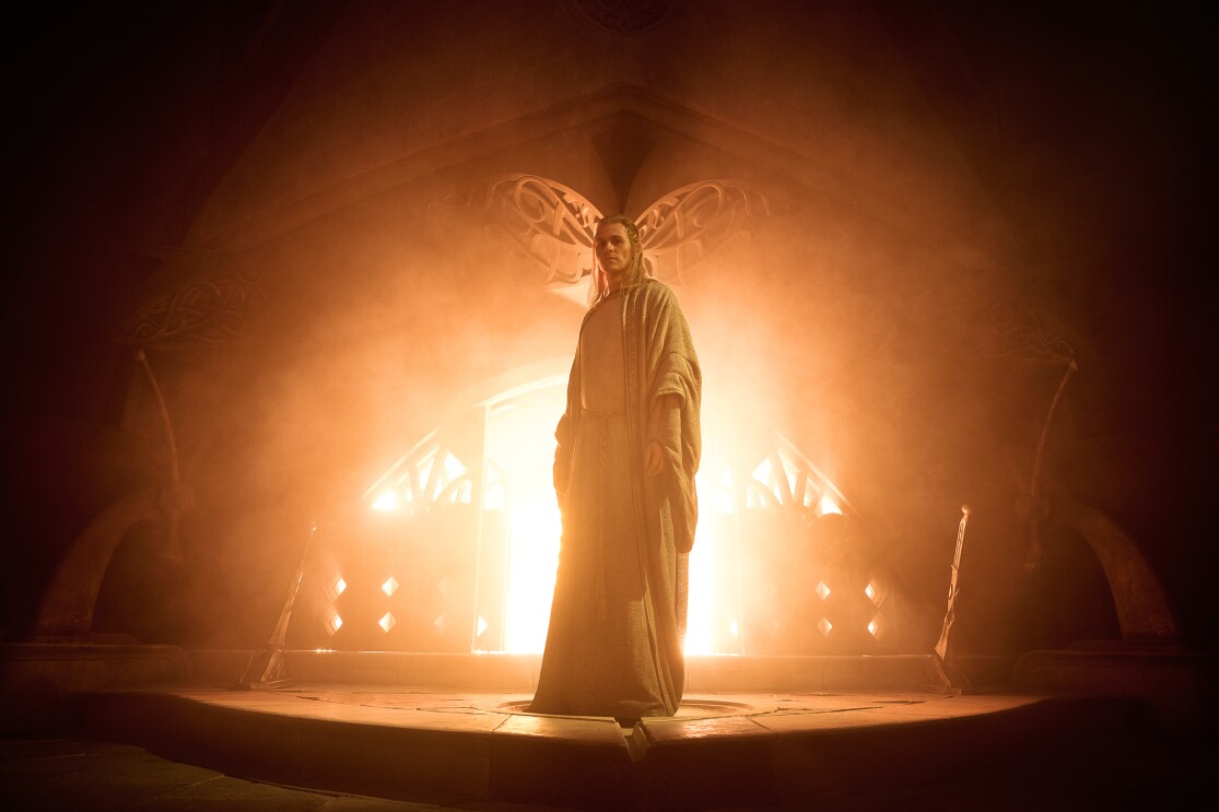 背後からオレンジ色の光に包まれる人物。ローブをまとい、長い髪を束ねている