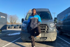 Jaren wears his Amazon jacket and stands in front of one of his Amazon delivery vehicles.