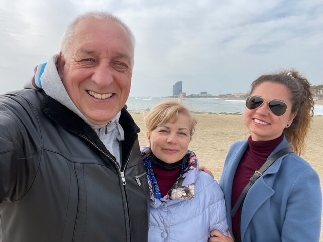 Daria and parents smile for a picture on a beach in Spain.