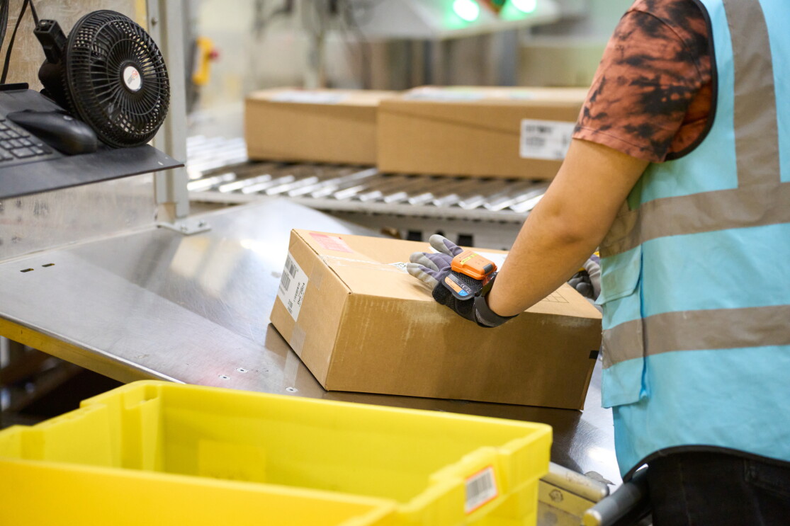 An Amazon fulfillment centre employee scanning a package on a conveyor belt
