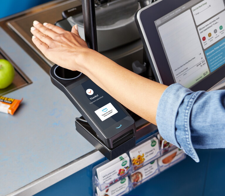 A hand hovers over a scanner at a grocery store, allowing a woman to check out and purchase her items.