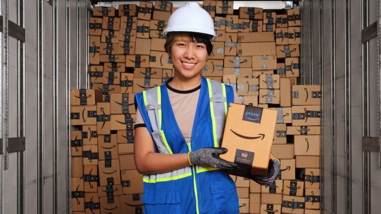 Amazon warehouse worker holding Prime package amid stacks of boxes