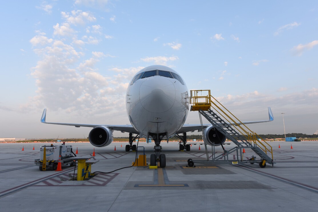 An image of the front of a Prime Air plane. There are stairs leading up to the cockpit and other equipment around the plane.