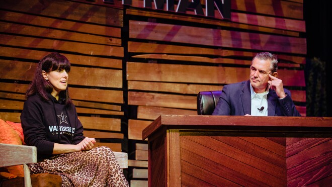 亚马逊的Maria Renz穿着Vanderbilt运动衫和动物印花裙子。她坐在莱曼酒店的舞台上,旁边是一张桌子,凯文·奥马拉坐在桌子后面。他们进行交谈。