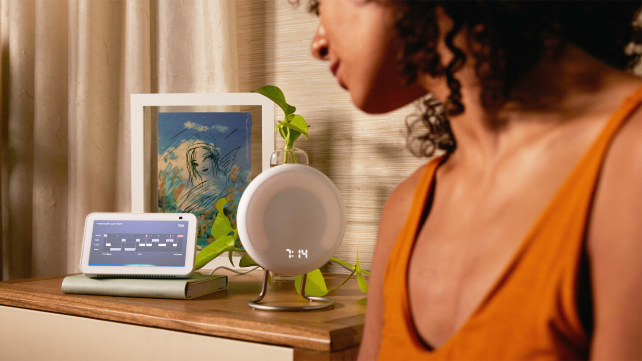 An image of a person looking at an Amazon Echo device and a Halo Rise sitting on a nightstand. 