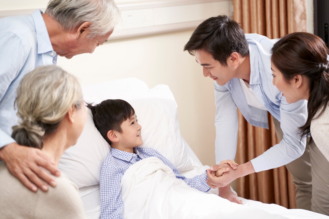 Child in bed in hospital ward gets a visit from parents and grandparents