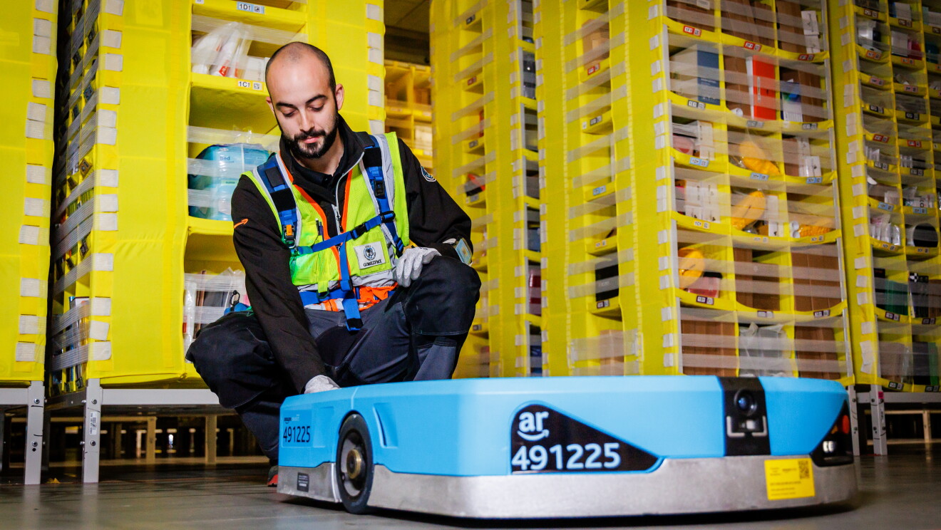 Dentro de un centro logístico un trabajador de Amazon arreglando un robot de Amazon. 