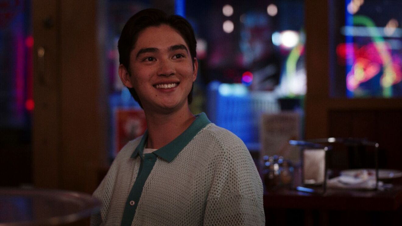 Smiling Steven Conklin (Sean Kaufman) in knit sweater at dimly lit restaurant