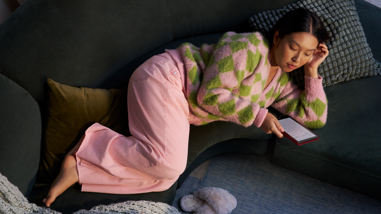 A woman lying on a sofa reading the Kindle Paperwhite
