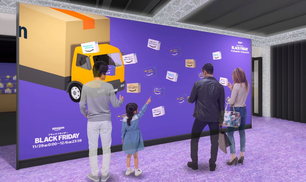 会場のイメージ図。大きなスクリーンにはAmazonのトラック、いくつかの箱が表示されている。そのスクリーンの前には男性2人、女性1人、そして女子1人がスクリーンを見ている