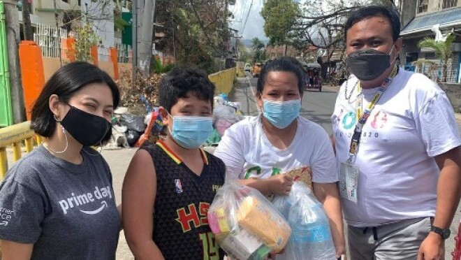 Two Amazon employees pose for a picture with a woman and her son who are both holding plastic bags full of food and water bottles.