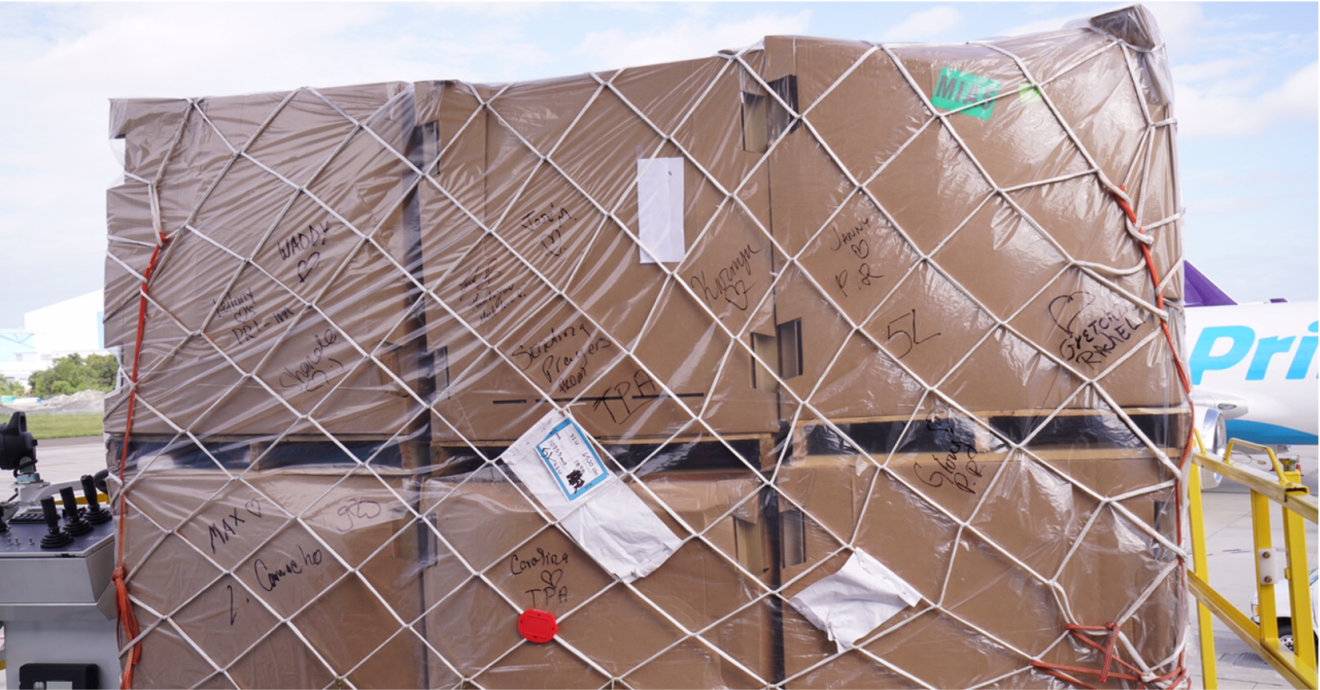 An image of several brown boxes stacked with clear wrapping over them. There are names written in black marker on the clear wrapping.