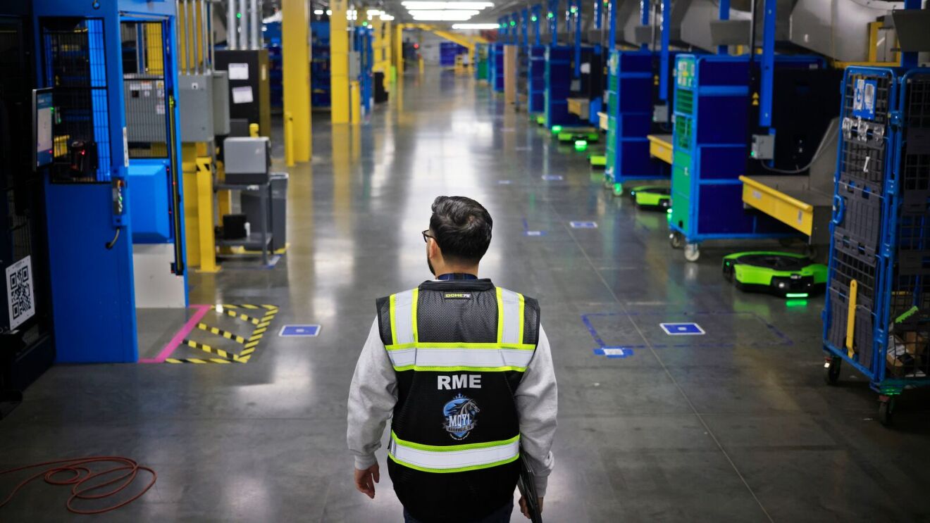 An Amazon employee at a fulfillment center, with robots parked toward the side.