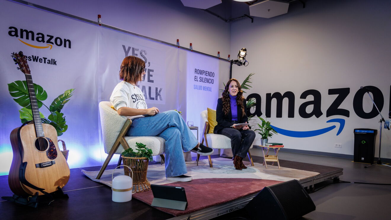 En un escenario creado para la ocasión, de fondo hay un cartel con el logo de Amazon y el Yes, we talk, que es el lema de la campaña. En el escenario hay una guitarra, tres plantes con sus respectivas macetas, dos mesas y dos sillas en las que están sentadas una trabajadora de Amazon a la que no se le la cara, solo unas deportivas negras, unos jeans de color azul y una sudadera blanca, está mirando a Mai Meneses, que está sentada en otra silla vestida con unos pantalones y una americana negros y un jersey de cuello alto de color violeta. 