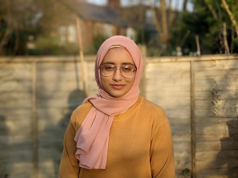 Zoya Anwar standing in a garden in front of a fence