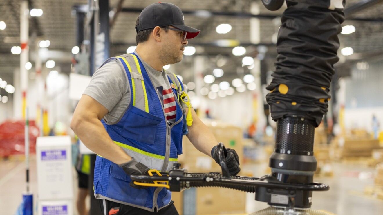 Employee in safety vest and cap using automated machinery in fulfillment facility