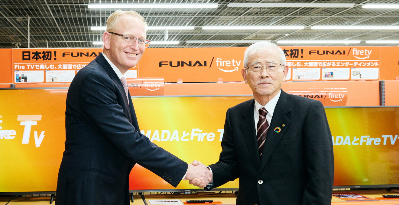 「FUNAI Fire TV搭載スマートテレビ」の前で笑顔で握手をするAmazon Device & Services担当、上級副社長のデイブ・リンプとヤマダホールディングスの山田昇会長