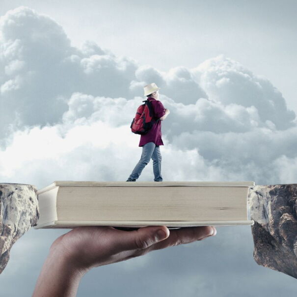A surreal image of a person walking across cliffs bridged by a book.