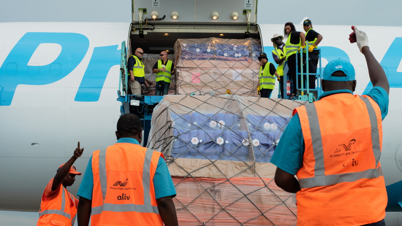 Employees in orange and yellow safety vests lift cargo supplies onto a Prime Air plane.  