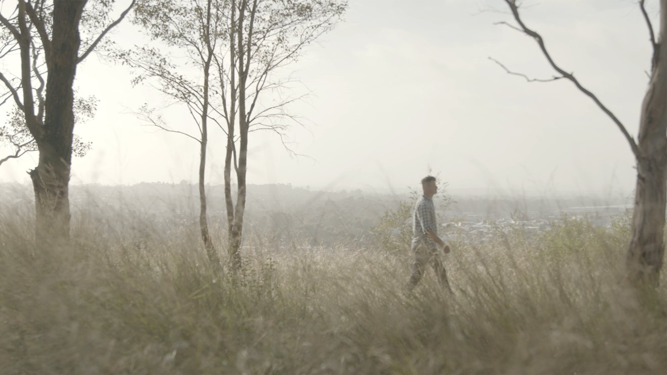 A man walks through the bush, the sky is hazy from the bush fires. 