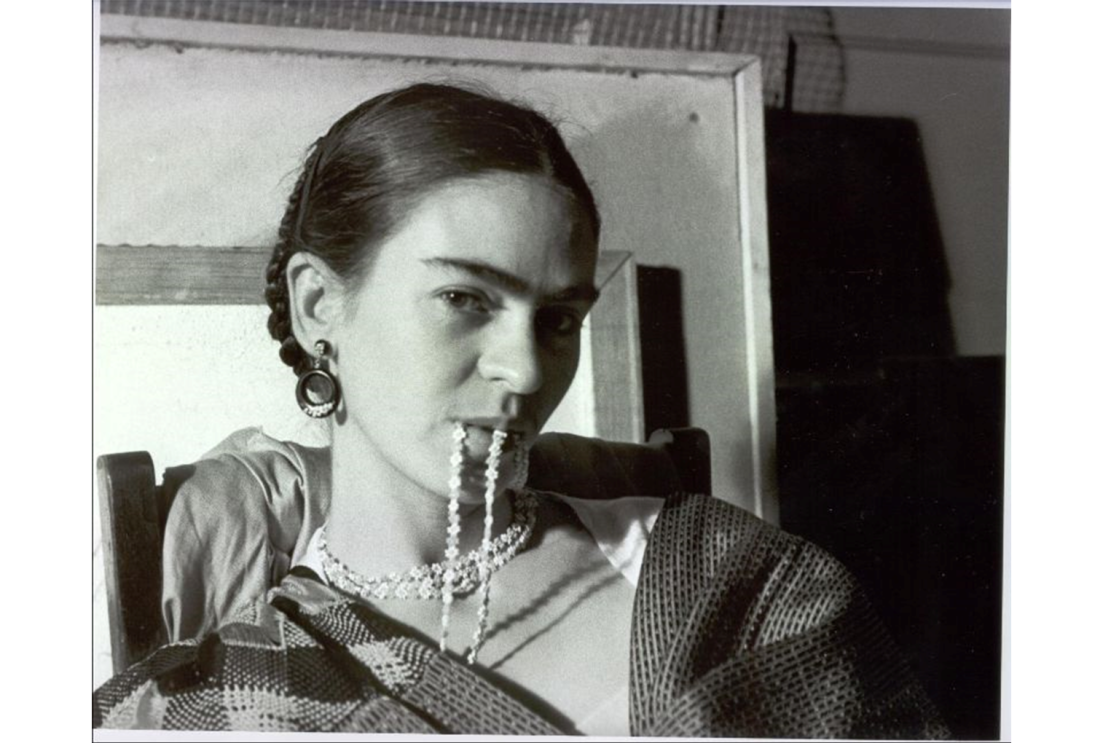 A woman with slicked-back hair do is biting necklace shown in black and white image. Frida Kahlo.