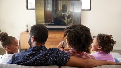 一家人坐在电视前,远程。两个孩子和两个大人微笑时点击照片在电视屏幕上显示出来。