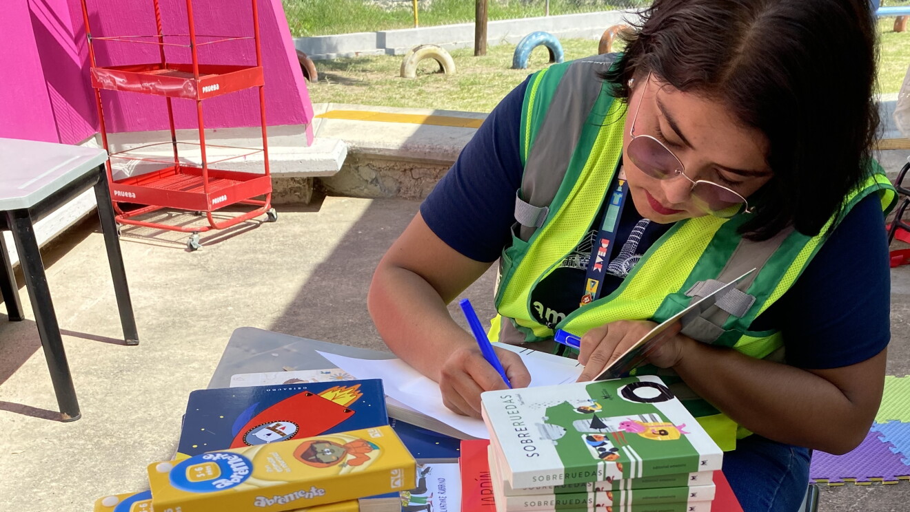 Voluntaria de Amazon entre libro en el patio de un colegio. 