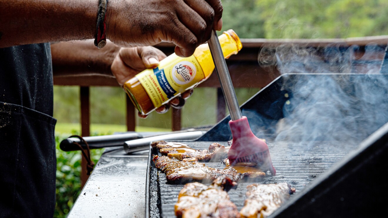 A photo of someone basting ribs on a barbeque with “Hab Mussy” hot mustard barbecue sauce by Lillie’s of Charleston.