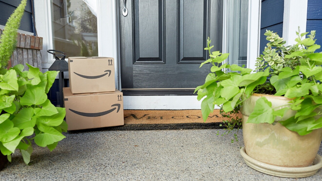Two Amazon boxes or packages stacked on a door mat on a front step. 