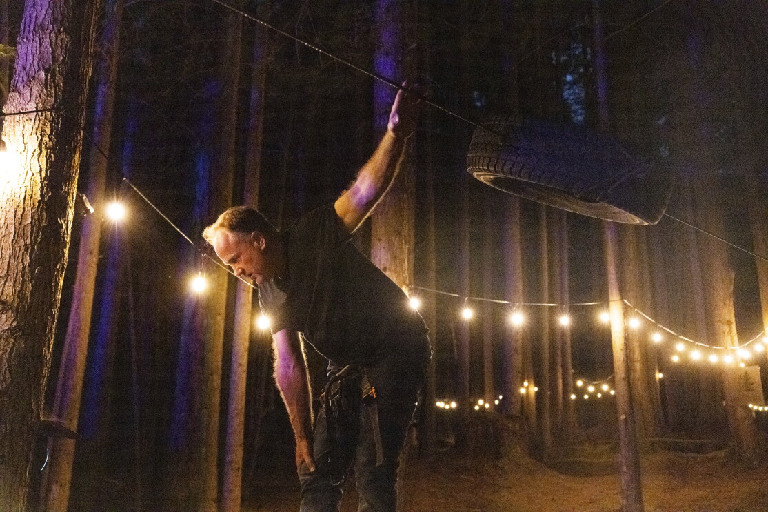 A man in a forest with strings of lights behind him.