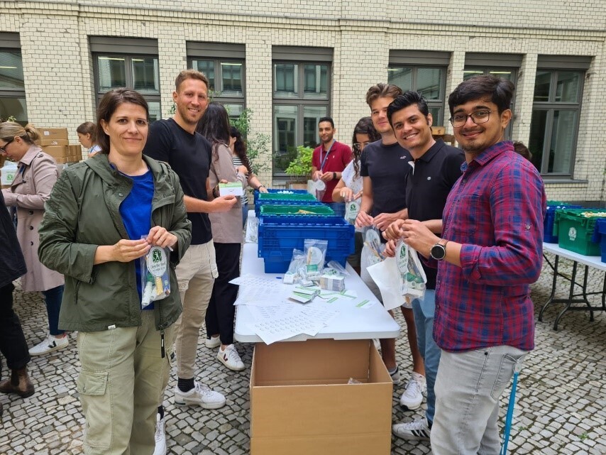 Man sieht eine Gruppe von Amazon Mitarbeiter:innen, die Hygiene-Kits in den Händen halten und in die Kamera lächeln.