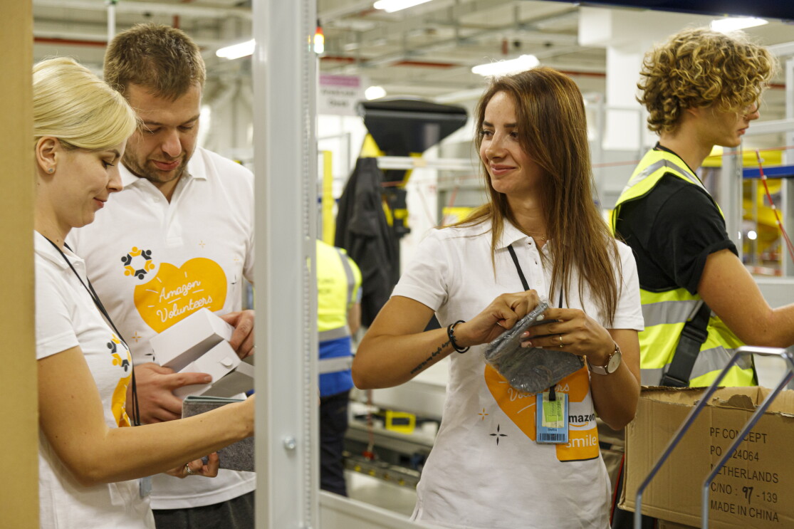 3 Mitarbeiter in T-Shirts mit Aufdruck "Amazon Volunteers" beim Packen.