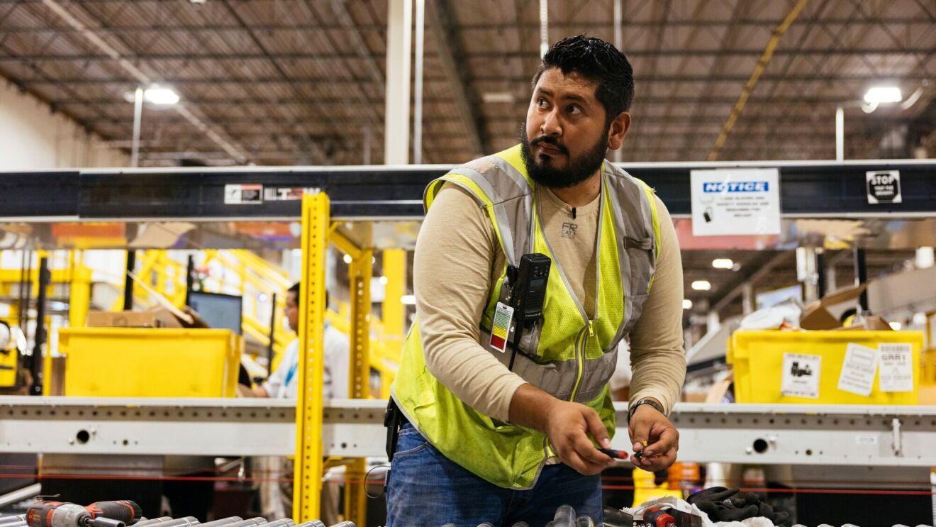 A photo of an employee working at a belt within an Amazon fulfillment center.