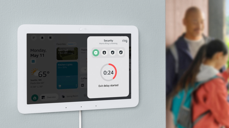 Amazon Echo Hub smart home security panel mounted on wall displaying arming status with family visible in background
