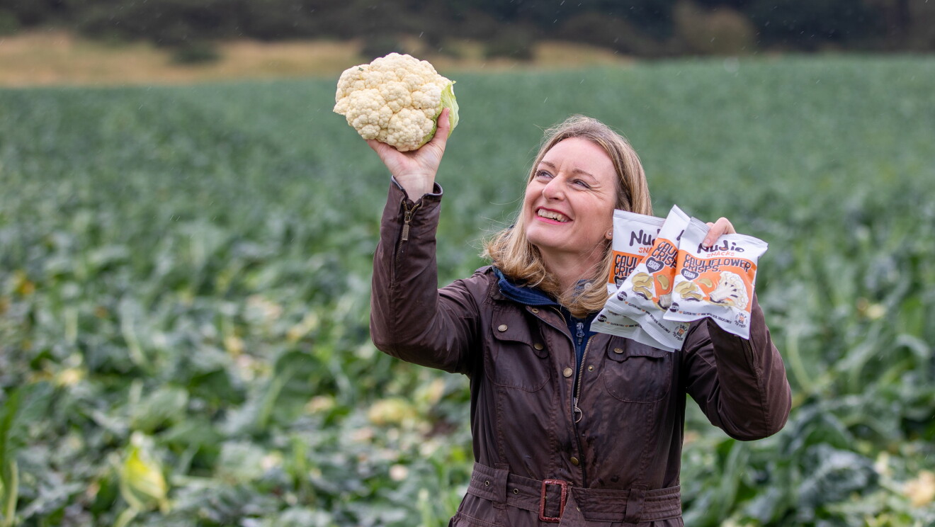 Business owner holding up a cauliflower and nudie snacks