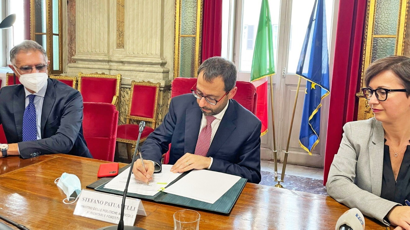Il Ministro delle Politiche Agricole, Stefano Patuanelli, firma un protocollo di intesa con accanto Mariangela Marseglia. Alle sue spalle le bandiere dell'Italia e dell'Unione Europea