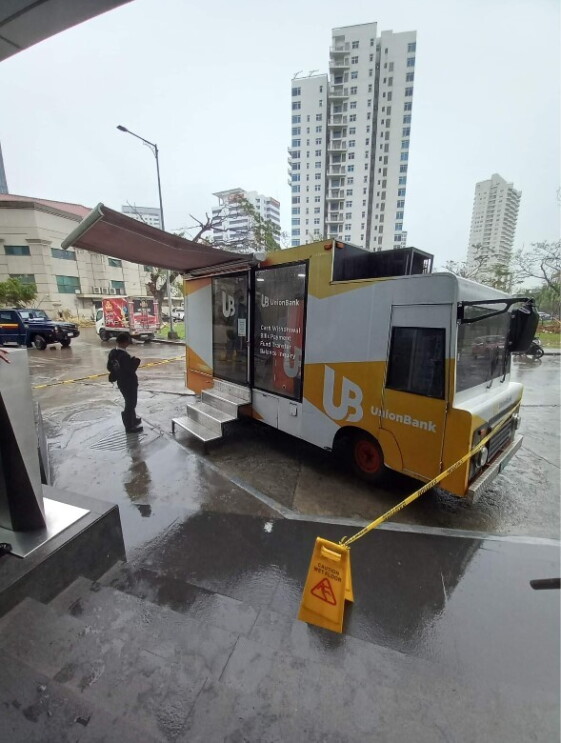 A van with an ATM on board. A lady is standing outside and looking at her mobile phone.