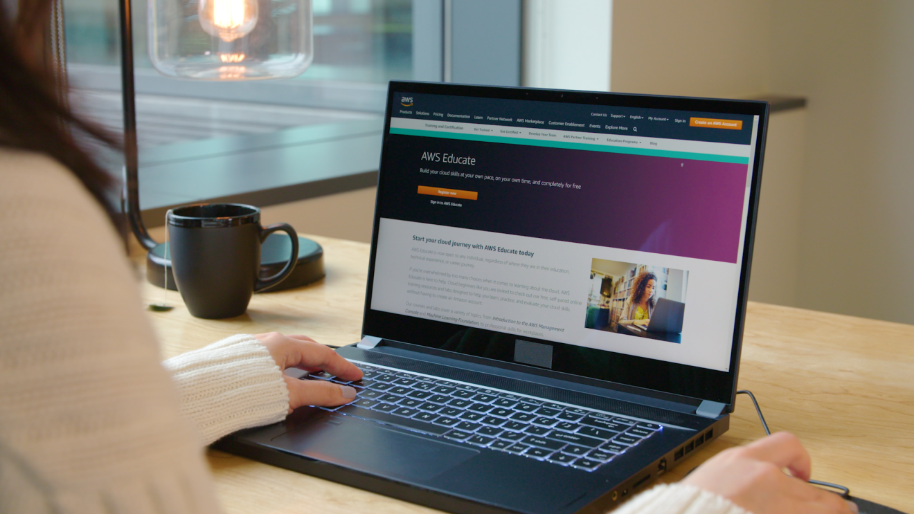 A laptop with AWS Educate program on the screen. A woman's hands are on the keyboard and mouse.