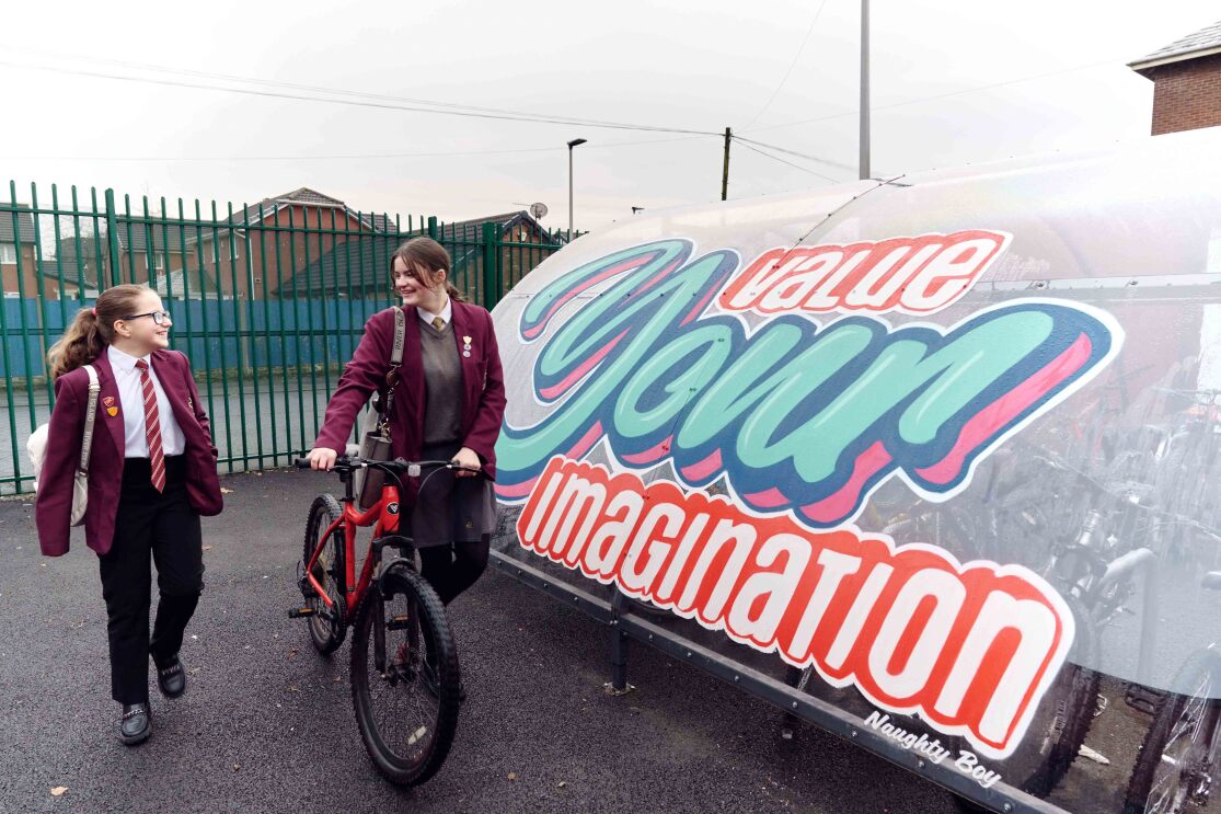 Student take their bikes past a Naughty Boy quote