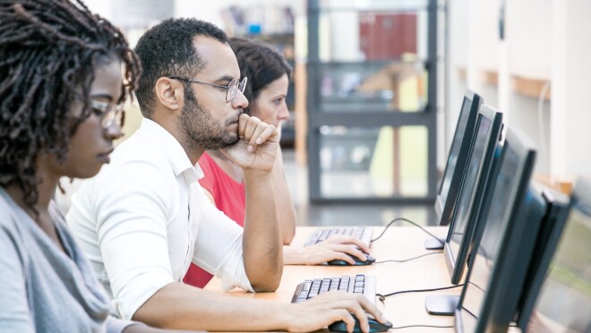 两个女人和一个男人坐在一张桌子与个人电脑专注于自己的显示器。