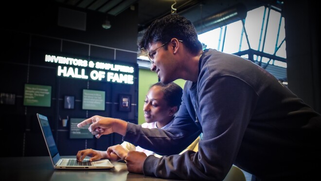 两个人正在看电脑屏幕。男人指着屏幕,女人在打字。