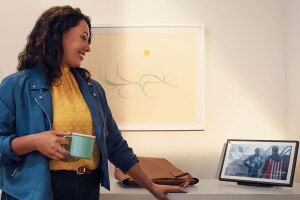 A woman holding a mug looking at her Echo device.