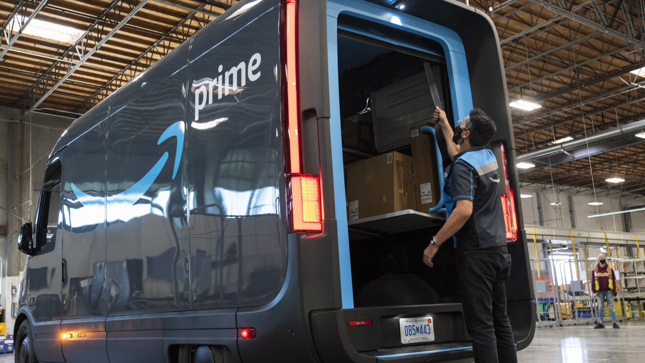 An Amazon delivery driver closes the back door of a Prime-branded Rivian van.