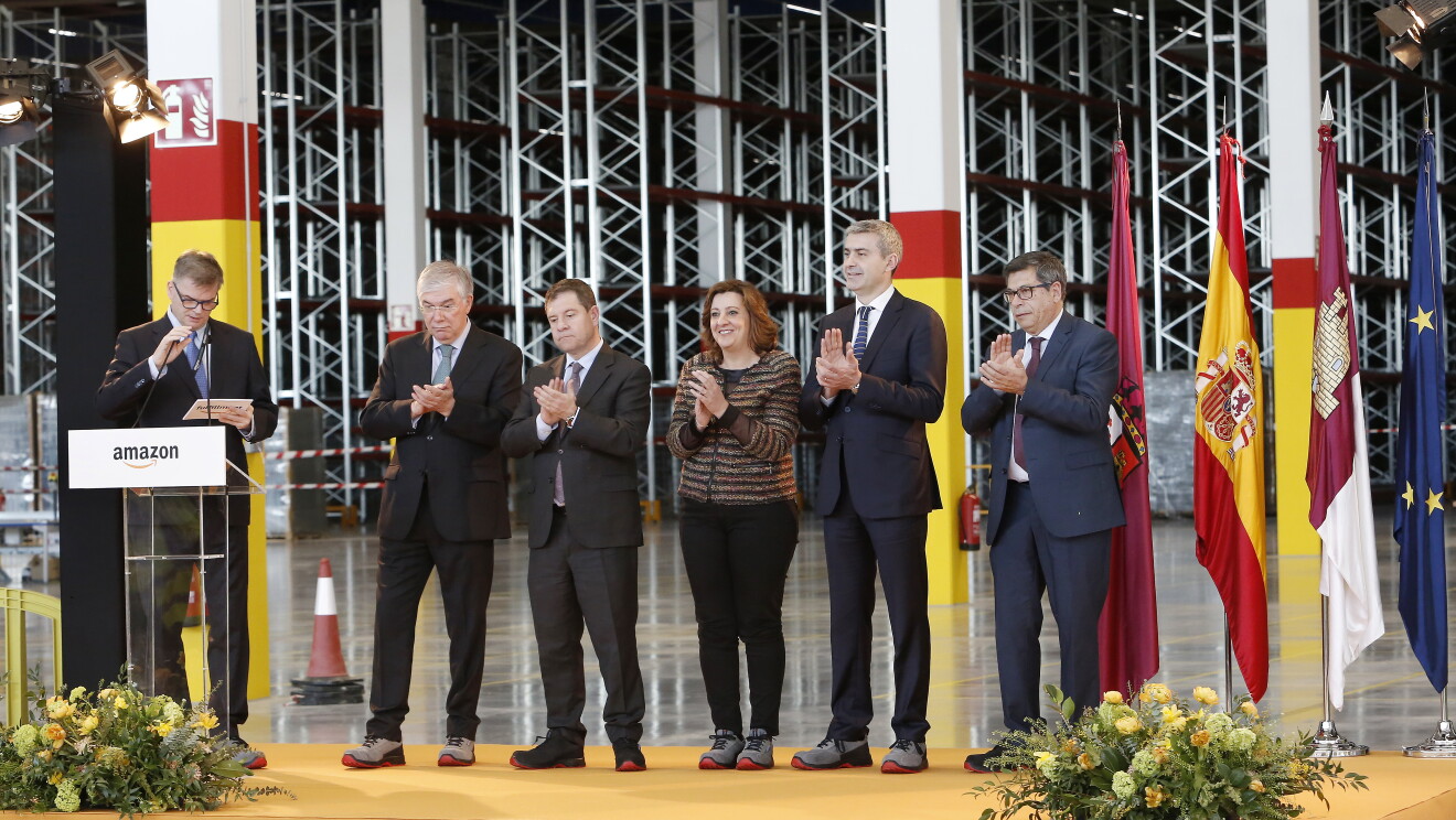 Visita oficial de las autoridades locales al centro logístico de Illescas. En una plataforma elevada y con las banderas correspondientes detrás aparecen el alcalde de Illescas, José Manuel Tofiño, y el presidente de Castilla-La Mancha, Emiliano García-Pagetodos. Hablando se encuentra el director regional de Operaciones en España e Italia de Amazon, Fred Pattje.