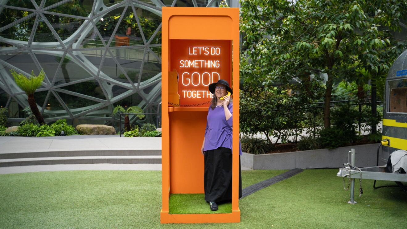 Person in purple shirt using bright orange phone booth with inspirational sign