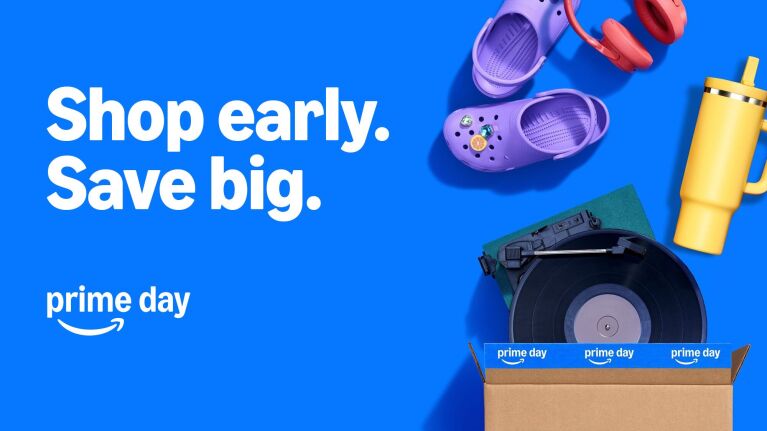 Amazon Prime Day promotional banner with purple Crocs, headphones, tumbler, and tape measure in cardboard box on blue background