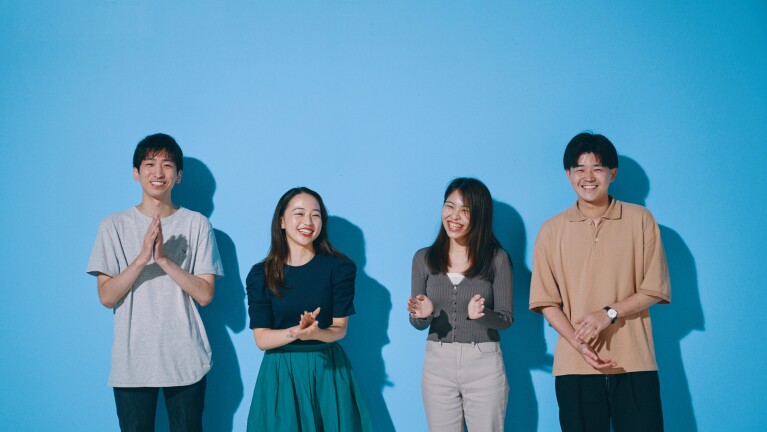 青い壁の前に男性二人と女性二人が笑顔で談笑している