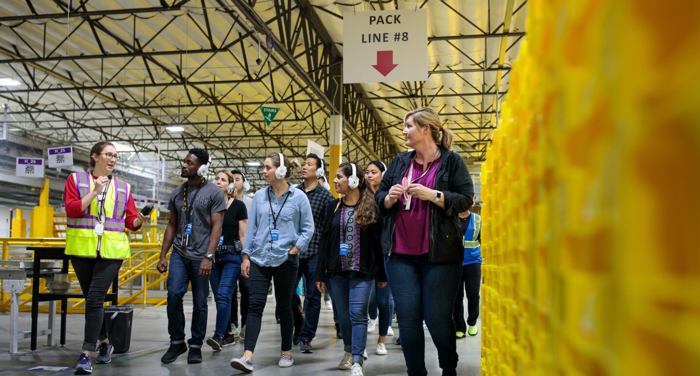 A photo of an Amazon employee give a guided walking tour of an Amazon Fulfillment center.