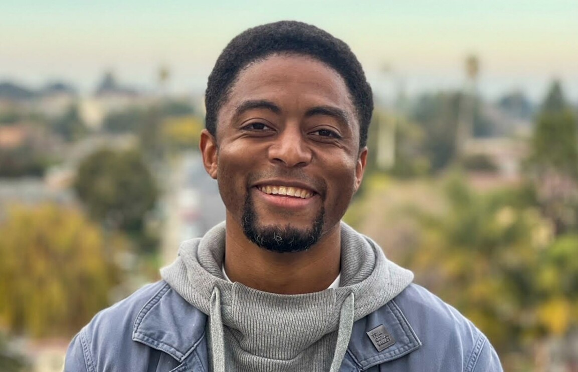 An image of a man smiling for a photo in front of a cityscape.