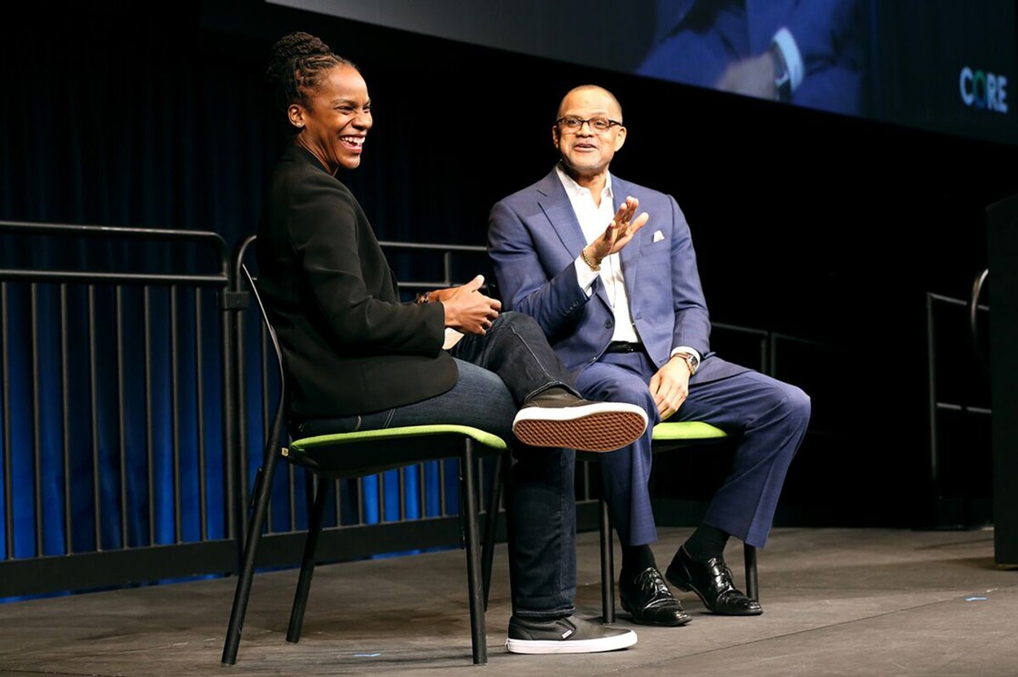 A woman in blue jeans and a black jacket smiles during a Q&A session onstage.